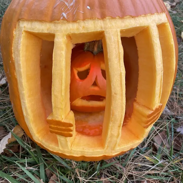 A small scared pumpkin locked behind carved jail bars inside a big pumpkin